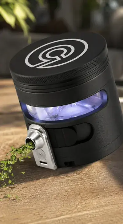 Black aluminum herb grinder with a lit viewing window and a metal dispensing spout, on a wooden table